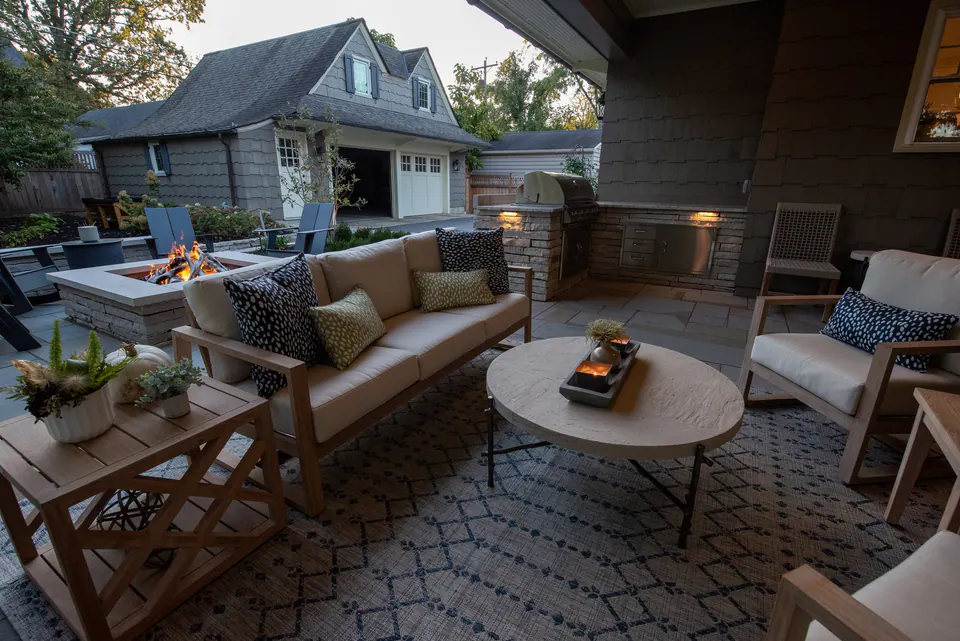 Covered patio lounge with sofa, chairs, paver terrace, fireplace wall, and house connection
